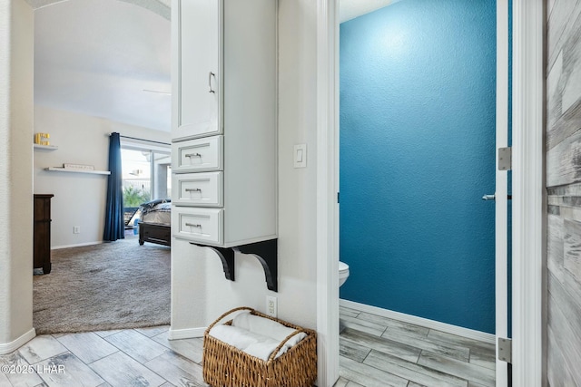 bathroom featuring toilet, a textured wall, baseboards, and wood finish floors