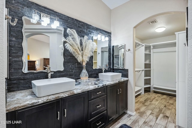 bathroom featuring wood finished floors, visible vents, backsplash, and a sink