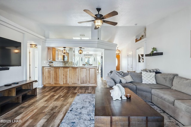 living room featuring arched walkways, dark wood finished floors, lofted ceiling, and ceiling fan