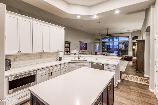 kitchen with light countertops, open floor plan, white cabinets, a sink, and a peninsula