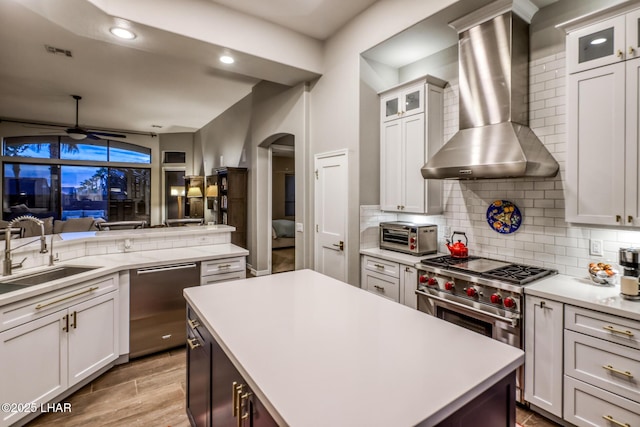 kitchen with stainless steel appliances, a sink, visible vents, light countertops, and wall chimney exhaust hood