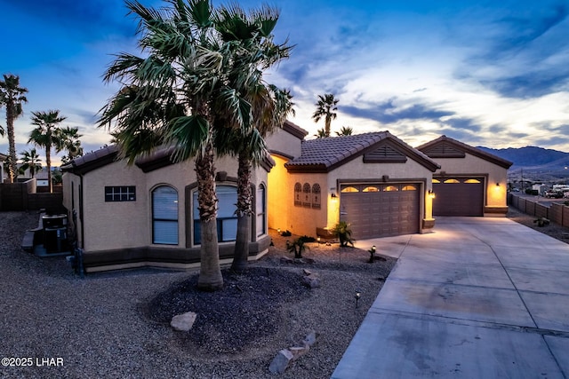 mediterranean / spanish home featuring an attached garage, driveway, a tiled roof, and stucco siding