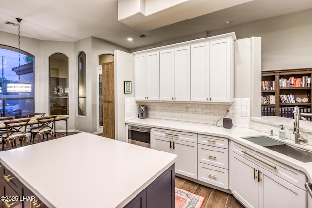 kitchen featuring white cabinets, decorative backsplash, dark wood-type flooring, light countertops, and a sink