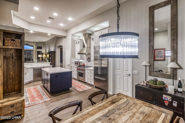 kitchen with arched walkways, high end appliances, light countertops, visible vents, and wall chimney range hood