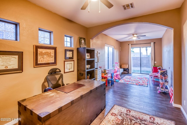 office space featuring baseboards, visible vents, arched walkways, ceiling fan, and wood finished floors