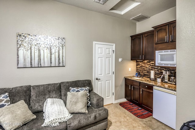 interior space featuring dark brown cabinetry, white appliances, visible vents, decorative backsplash, and stone counters