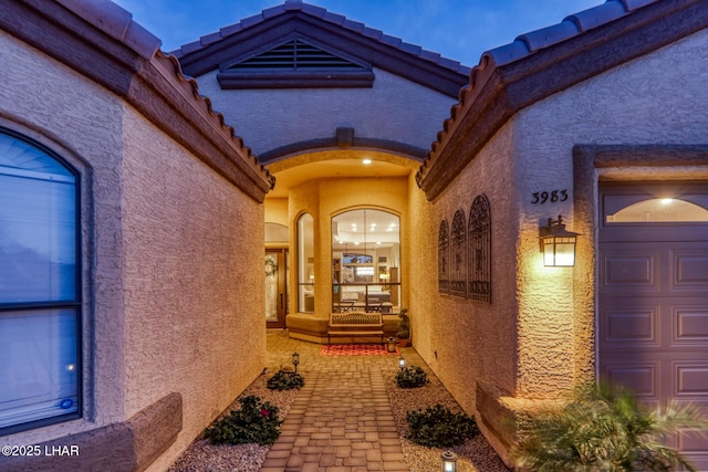 property entrance with a tiled roof, an attached garage, and stucco siding