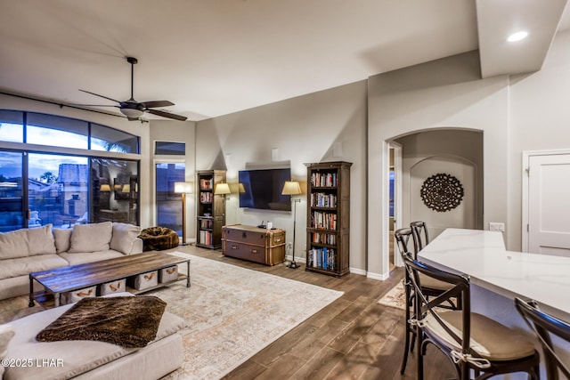 living room with dark wood-style floors, ceiling fan, baseboards, and arched walkways