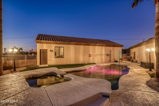 pool at dusk with a fenced in pool, a fenced backyard, a patio, and an in ground hot tub