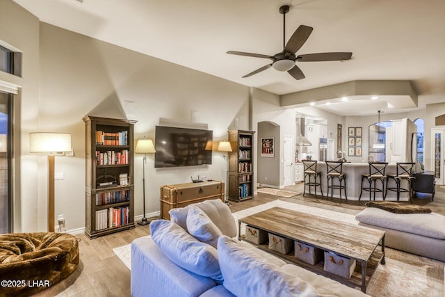 living area featuring arched walkways, ceiling fan, wood finished floors, and baseboards