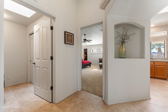 corridor featuring light carpet, light tile patterned flooring, and baseboards