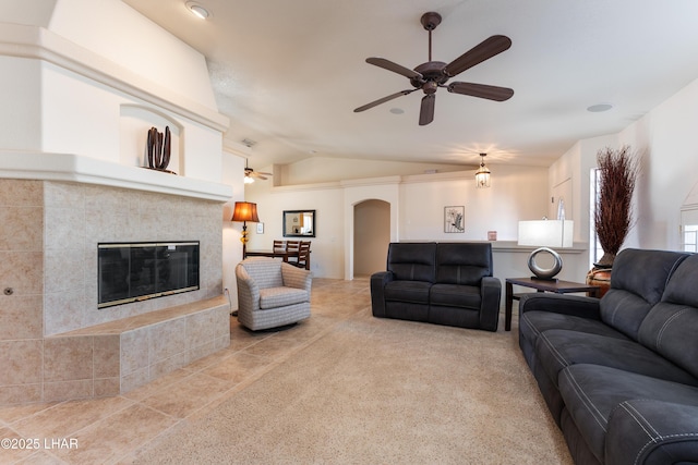 carpeted living room with arched walkways, vaulted ceiling, a tile fireplace, and a ceiling fan