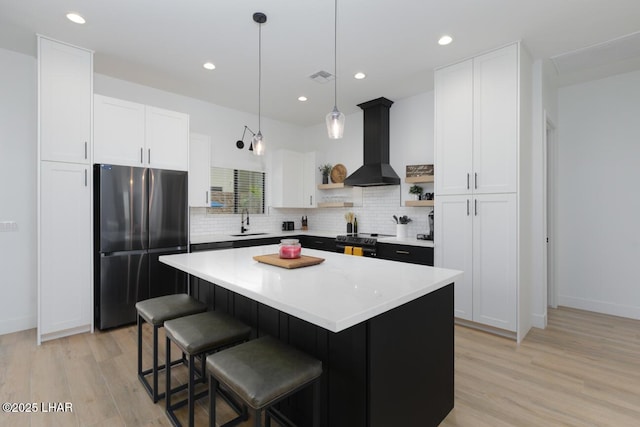 kitchen with freestanding refrigerator, open shelves, black electric range, wall chimney exhaust hood, and a sink