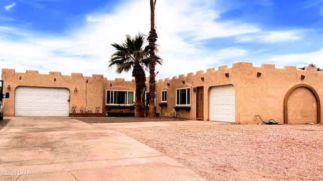 pueblo-style house featuring an attached garage, driveway, and stucco siding