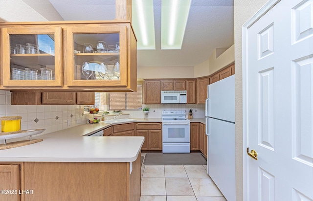 kitchen with white appliances, light tile patterned floors, a peninsula, light countertops, and a sink