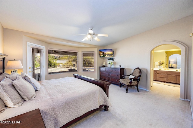 bedroom featuring arched walkways, lofted ceiling, ensuite bathroom, a ceiling fan, and light carpet