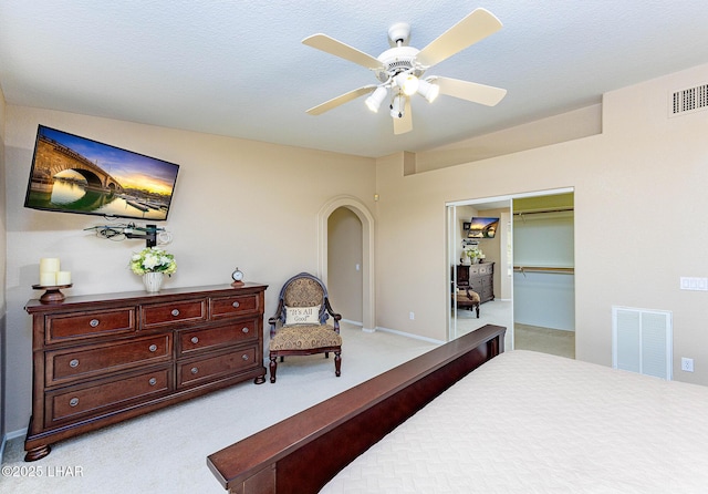 bedroom with ceiling fan, arched walkways, visible vents, and light colored carpet