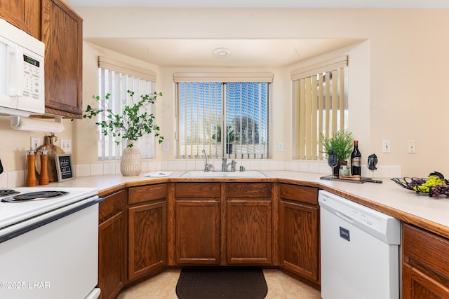 kitchen with a sink, white appliances, brown cabinets, and light countertops