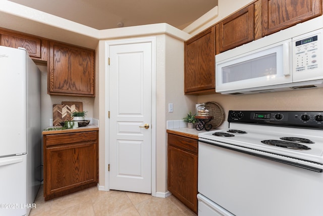 kitchen featuring white appliances, light tile patterned floors, baseboards, light countertops, and brown cabinets