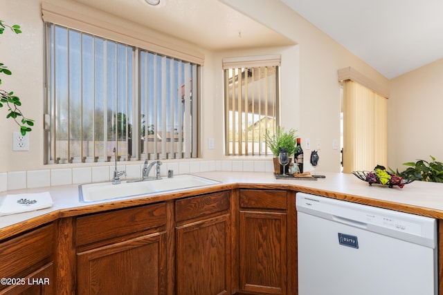 kitchen with a sink, brown cabinets, white dishwasher, and light countertops