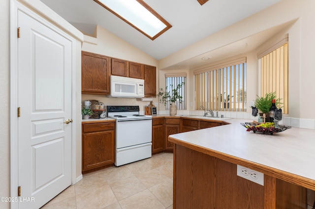 kitchen featuring white appliances, brown cabinetry, vaulted ceiling with skylight, a sink, and light countertops