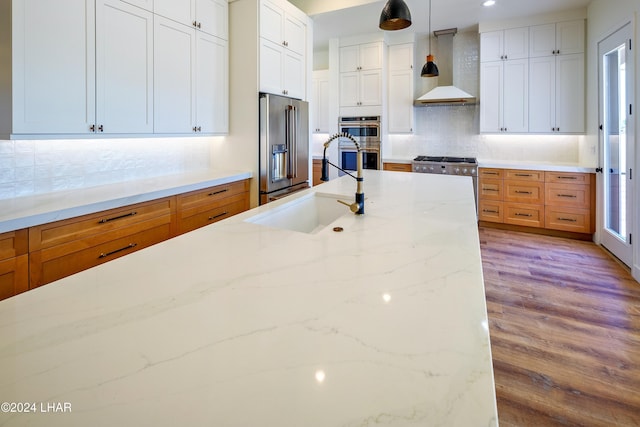 kitchen featuring decorative light fixtures, white cabinetry, high end appliances, light stone counters, and wall chimney exhaust hood