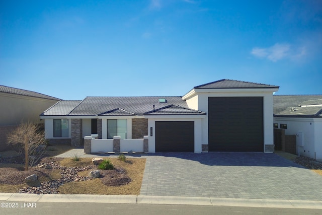 view of front facade featuring a garage, stone siding, a tiled roof, decorative driveway, and stucco siding