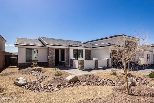 view of front of property with a tile roof, stucco siding, an attached garage, fence, and stone siding