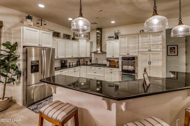 kitchen with pendant lighting, a breakfast bar area, wall chimney exhaust hood, and appliances with stainless steel finishes