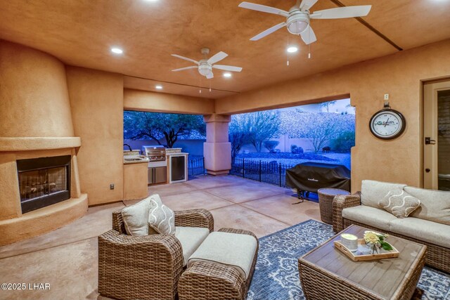 view of patio / terrace featuring ceiling fan, a grill, an outdoor living space with a fireplace, and exterior kitchen