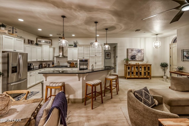 kitchen featuring decorative light fixtures, a breakfast bar, wall chimney exhaust hood, and appliances with stainless steel finishes