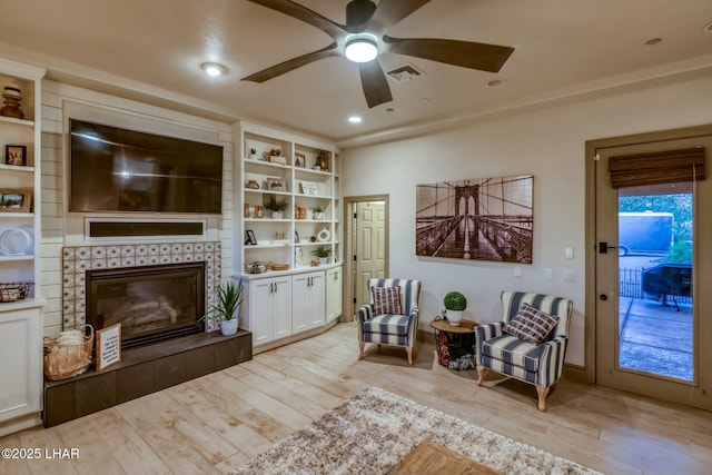 sitting room featuring a tile fireplace, ceiling fan, and light wood-type flooring