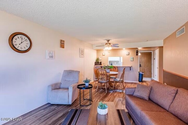 living room featuring hardwood / wood-style flooring, ceiling fan, and a textured ceiling