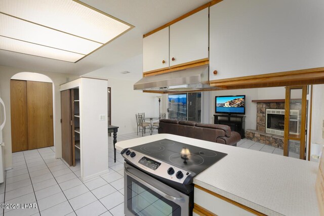 kitchen featuring a stone fireplace, light tile patterned floors, stainless steel electric range, and white cabinets