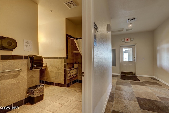 bathroom featuring visible vents, tile walls, and stone tile floors