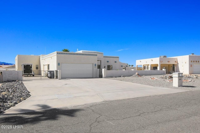 pueblo-style home with concrete driveway, a fenced front yard, an attached garage, a gate, and stucco siding