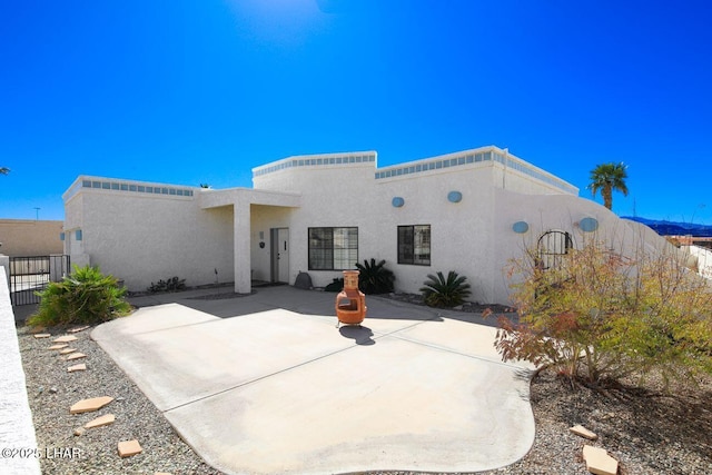 rear view of house with a patio area, fence, and stucco siding