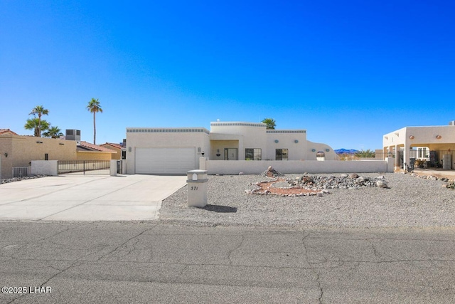 pueblo-style house featuring fence, driveway, an attached garage, and stucco siding