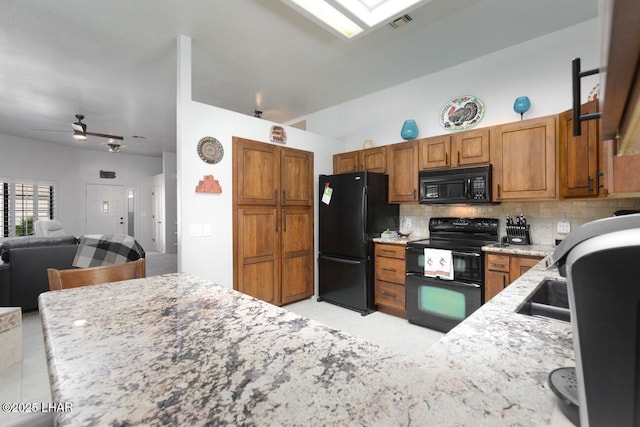 kitchen with light stone counters, decorative backsplash, brown cabinetry, ceiling fan, and black appliances