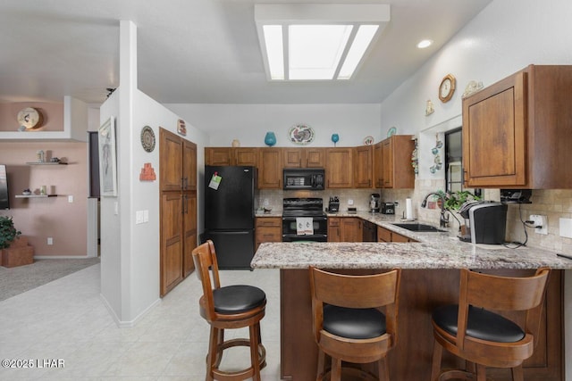 kitchen featuring a peninsula, a sink, brown cabinets, light stone countertops, and black appliances