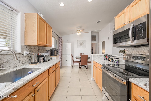 kitchen featuring sink, vaulted ceiling, light tile patterned floors, stainless steel appliances, and light stone countertops