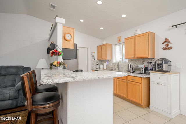 kitchen with lofted ceiling, light brown cabinetry, light stone counters, light tile patterned floors, and decorative backsplash