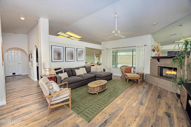 living room with baseboards, arched walkways, a tiled fireplace, hardwood / wood-style flooring, and a textured ceiling