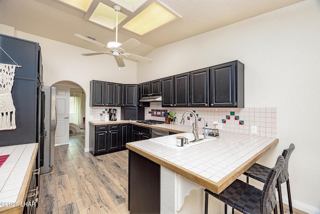 kitchen with tile countertops, arched walkways, gas cooktop, a peninsula, and a sink