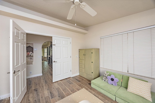 unfurnished living room with arched walkways, wood finished floors, a ceiling fan, and baseboards