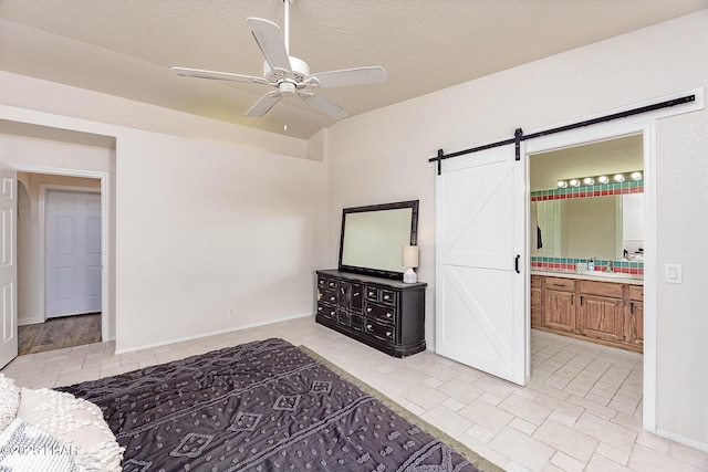 bedroom featuring ensuite bathroom, a barn door, ceiling fan, a sink, and a textured ceiling