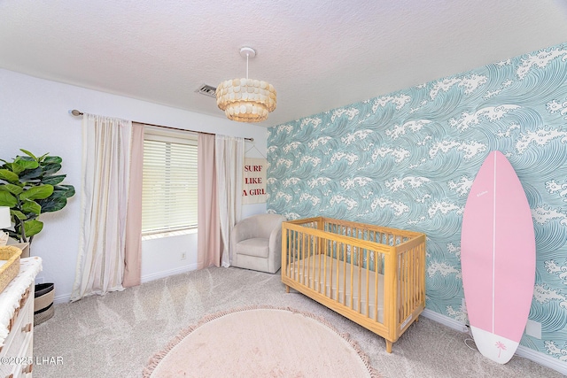 bedroom featuring carpet floors, visible vents, a textured ceiling, a crib, and baseboards