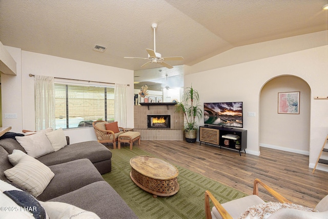 living room with arched walkways, a fireplace, visible vents, vaulted ceiling, and wood finished floors