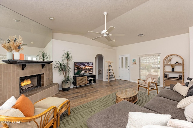 living area with visible vents, arched walkways, wood finished floors, vaulted ceiling, and a fireplace