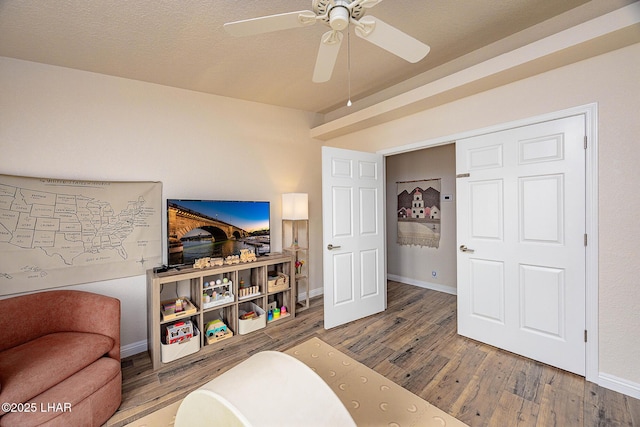 living area featuring a ceiling fan, a textured ceiling, baseboards, and wood finished floors